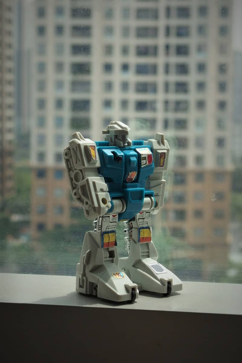Robot toy stands on a windowsill overlooking a city.