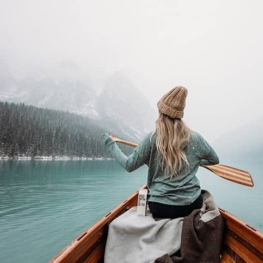 woman in gray long sleeve shirt sitting on brown wooden boat on body of water during