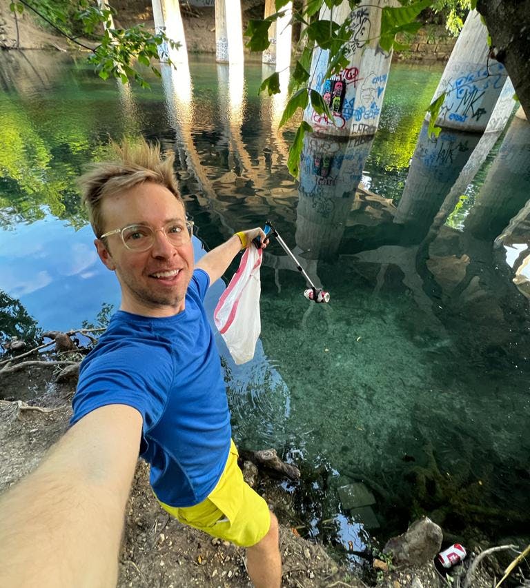 a selfie of Nick picking up garbage beside the creek using garbage picker