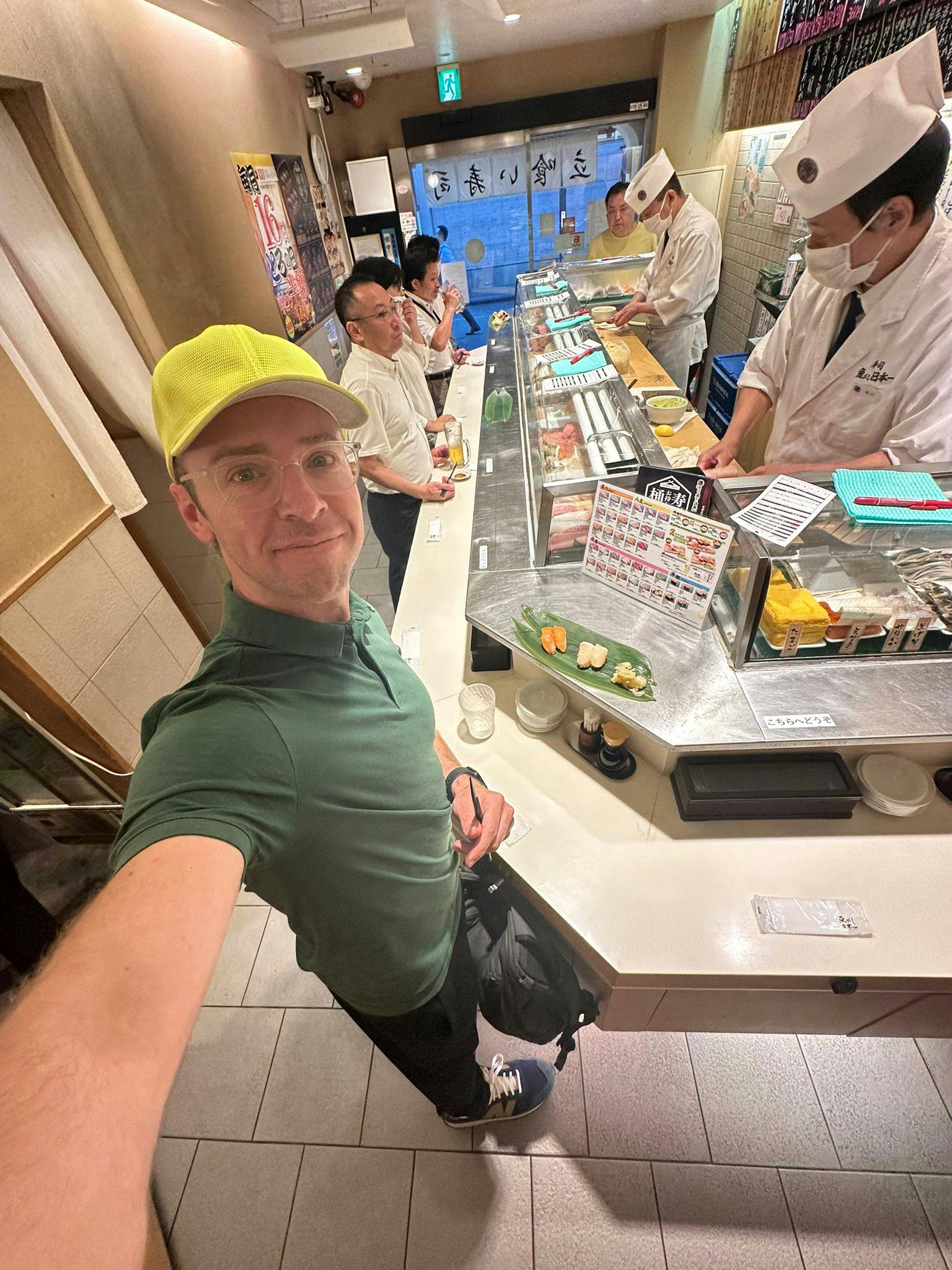 a selfie photo of Nick Gray standing at a standing sushi bar in Tokyo Japan