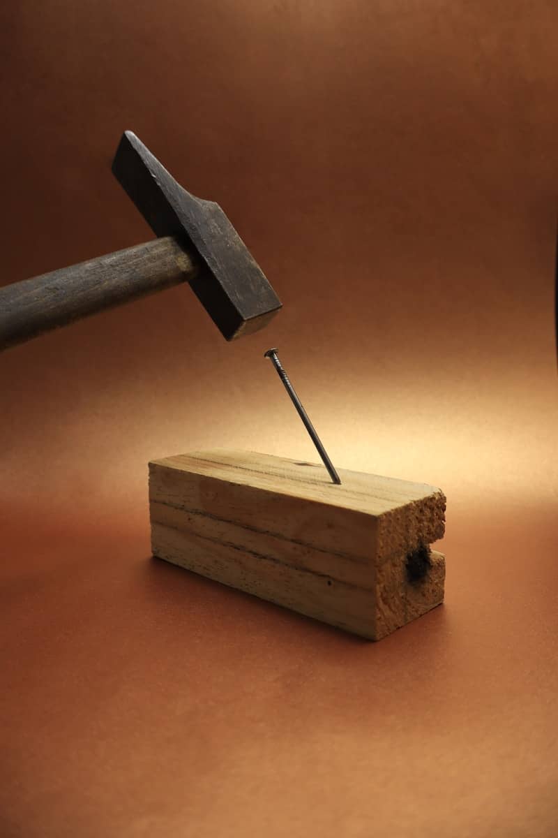 A hammer is driving a nail into wood.