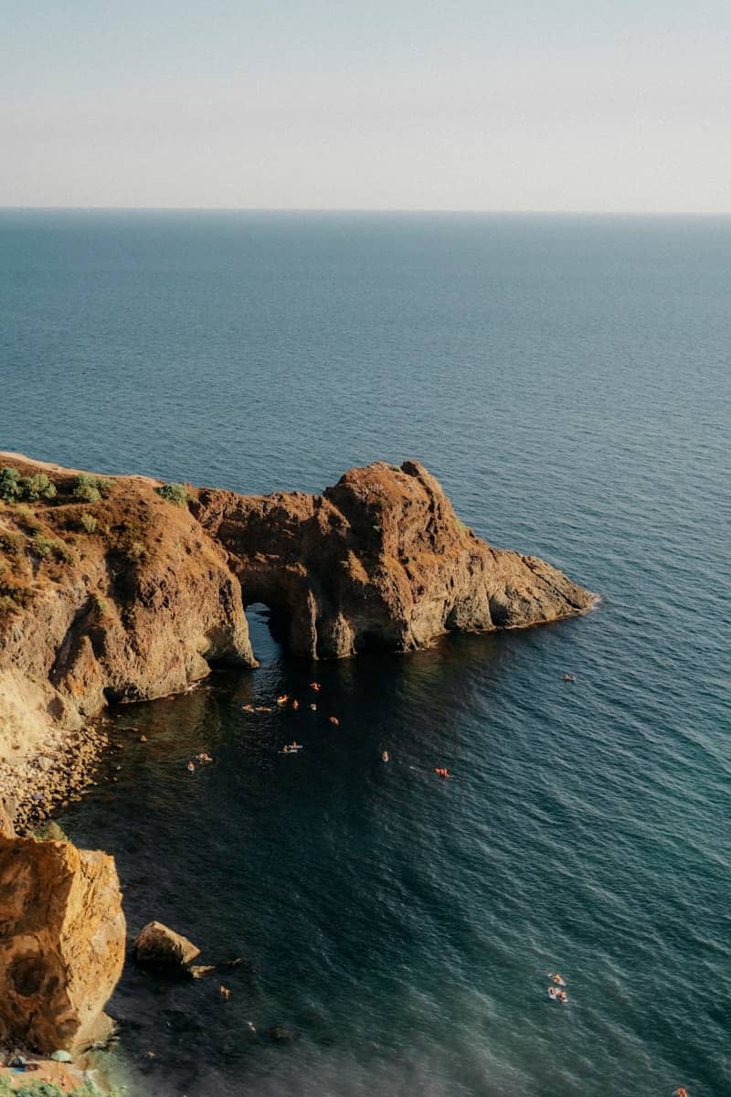 Kayakers explore a rocky archway on the coast.