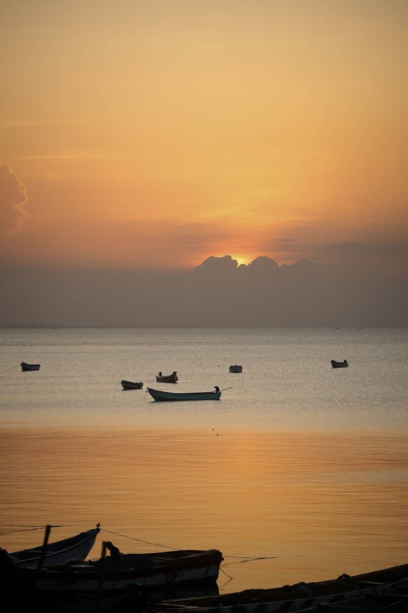 Several boats float on the calm ocean at sunset.