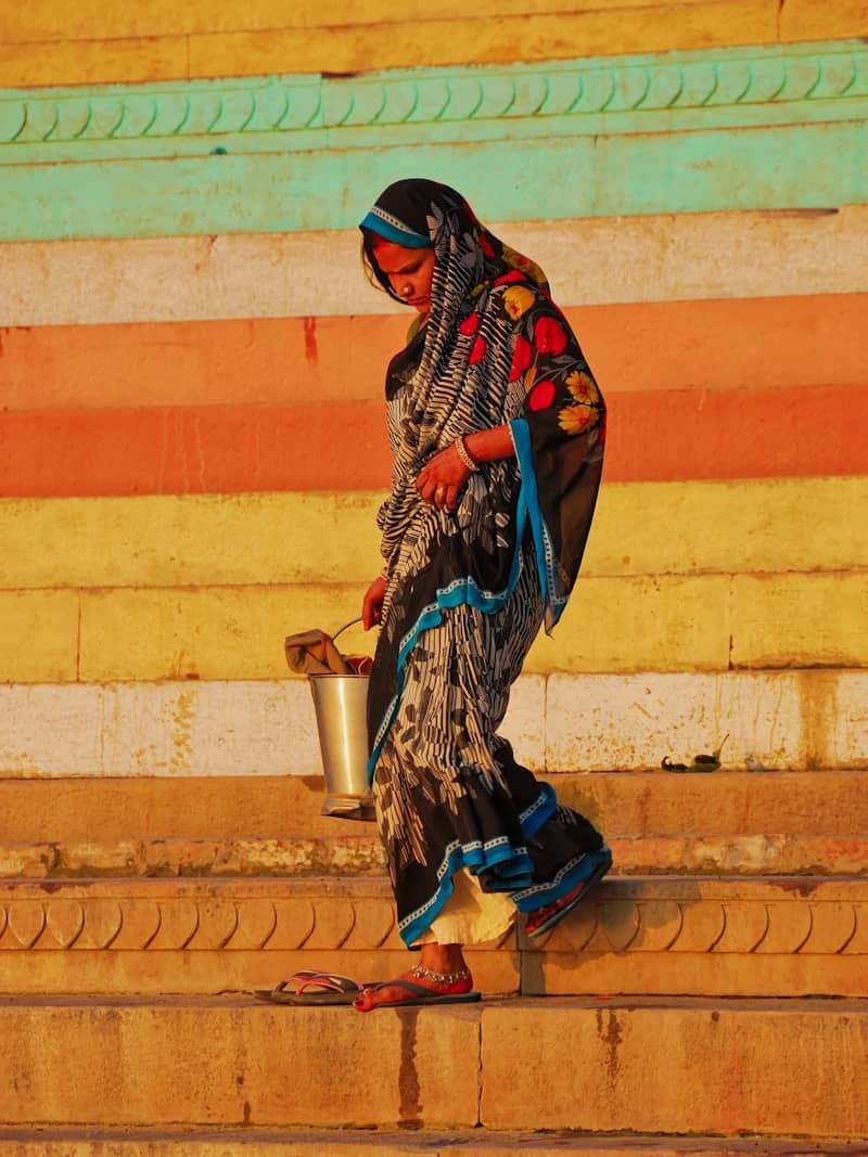 Woman in sari carries bucket down colorful steps.