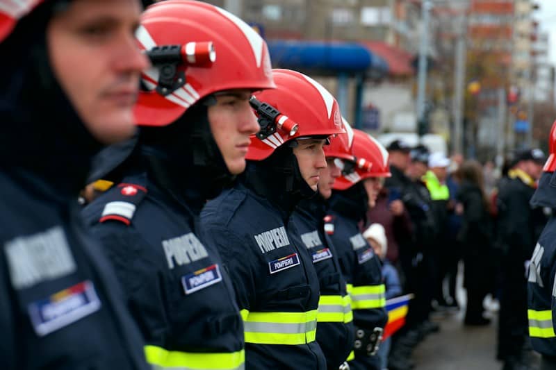 Firefighters in red helmets and dark uniforms standing in a line outdoors