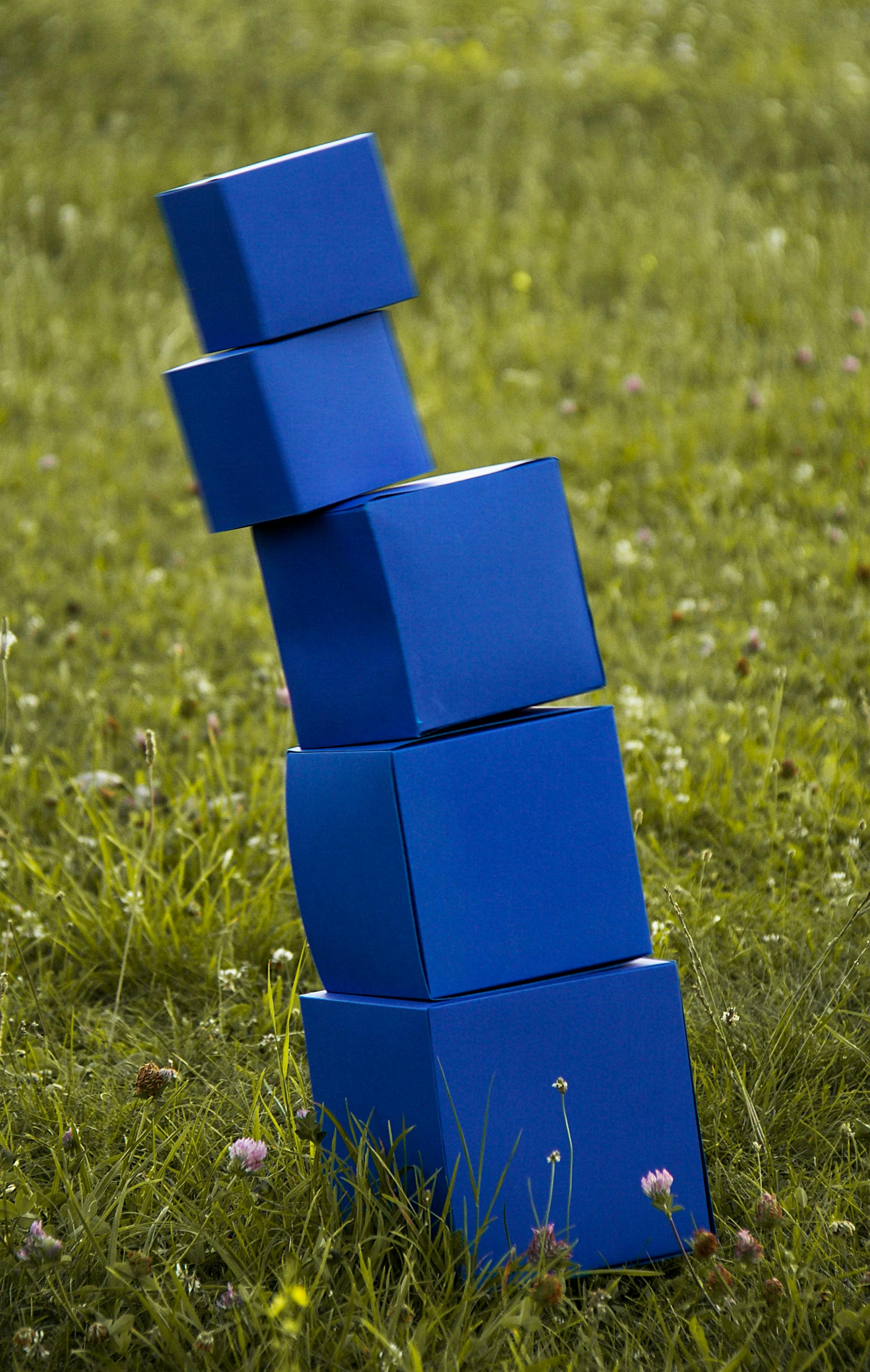 A stack of blue blocks ready to topple onto a green grass field