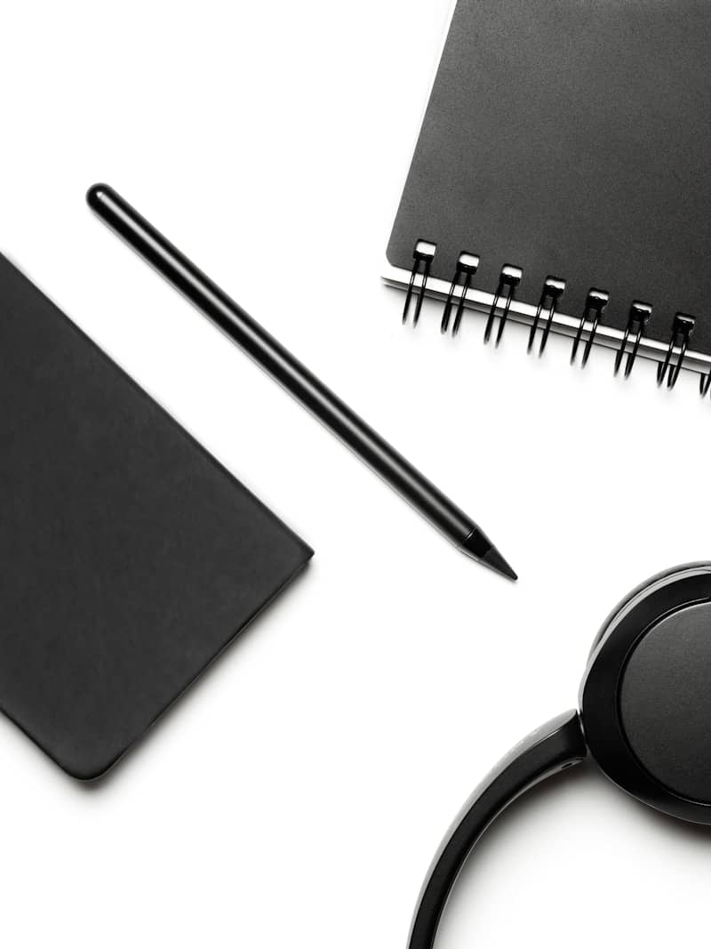 Black notebooks, pen, and headphones on a white surface.