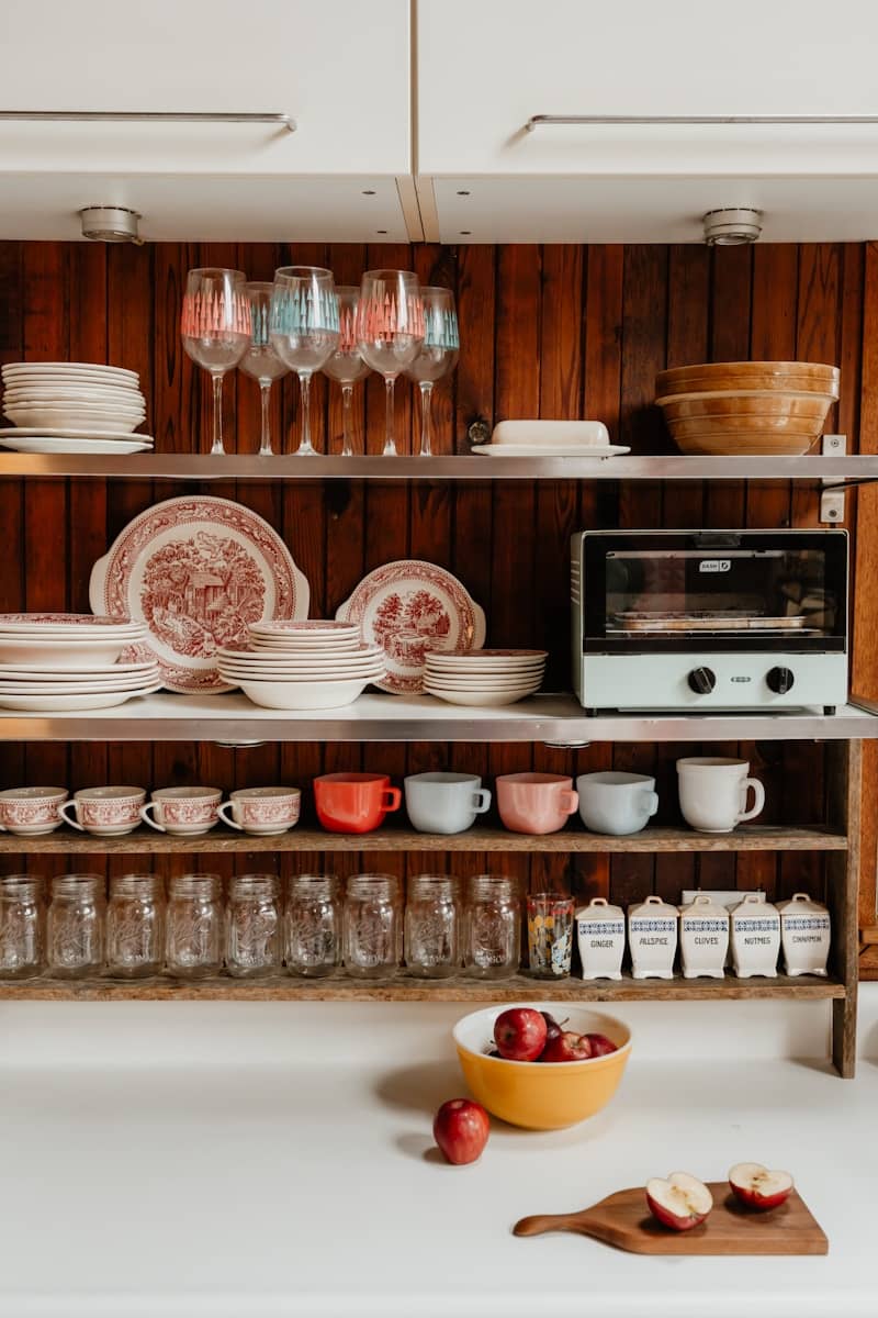 A kitchen shelf displays dishes, glasses, and jars.