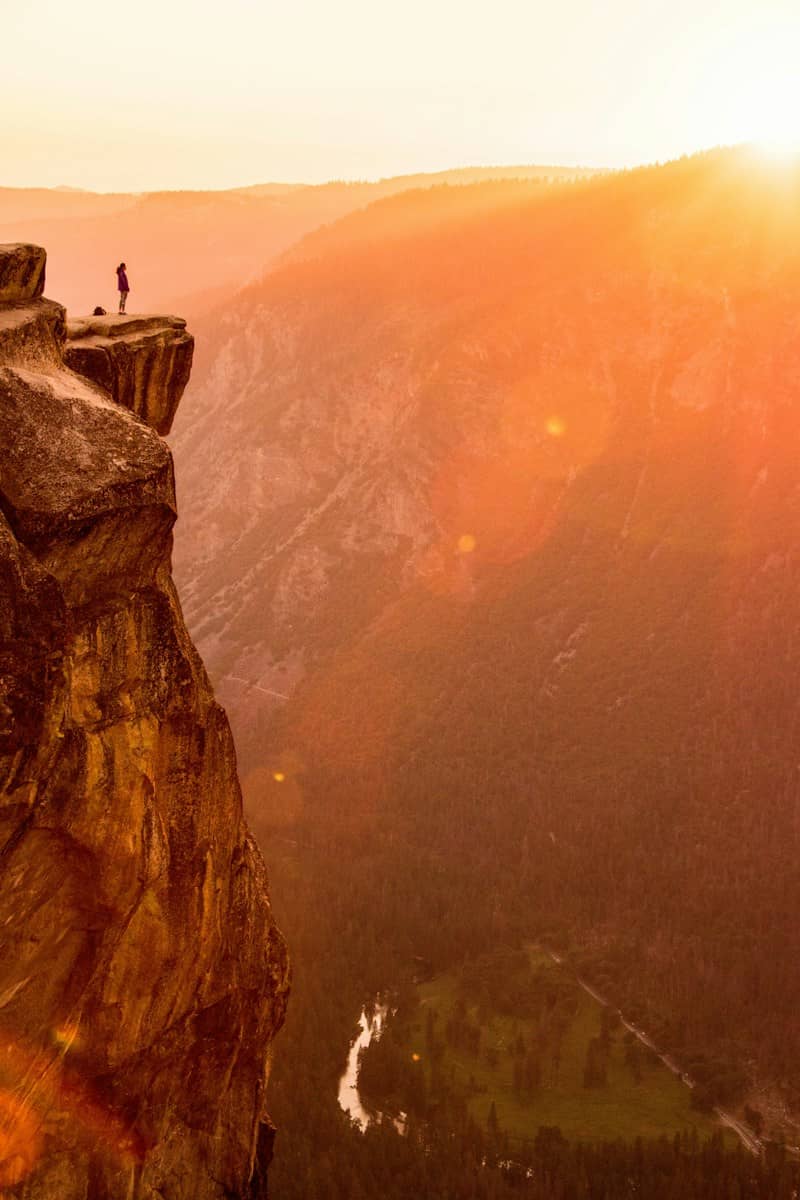 A person on a rocky cliff edge overlooking a deep valley in golden light