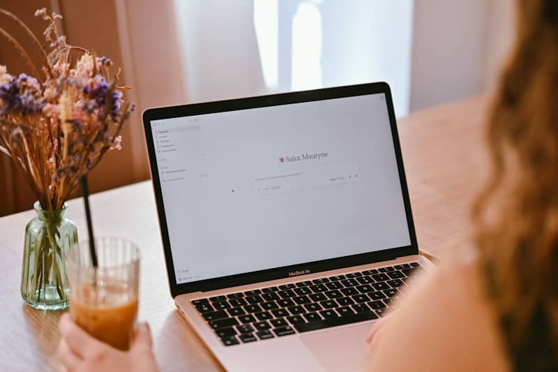 A person using a laptop with a dried flower bouquet and iced coffee