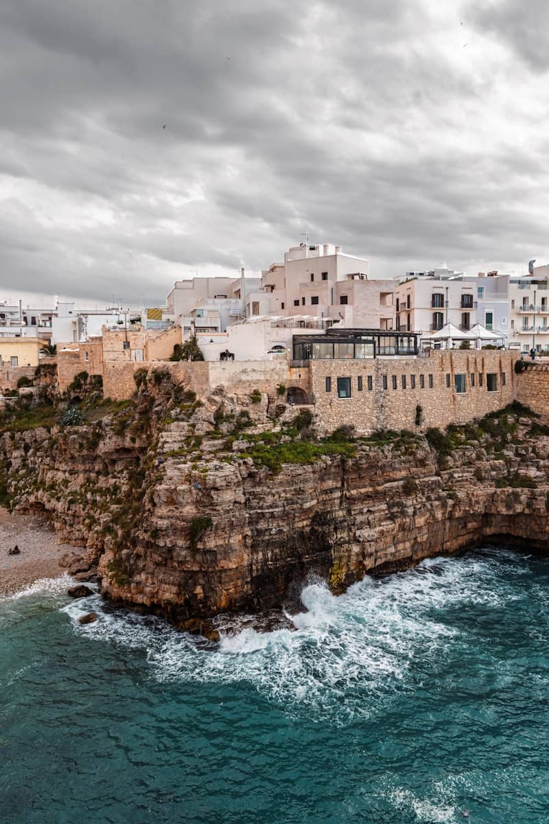 White buildings perch on a rocky cliff over the sea.