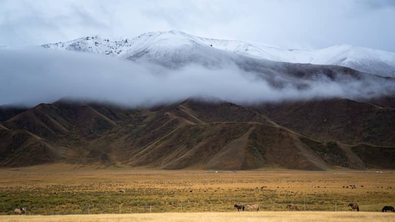 Snow-capped mountains shrouded in clouds above rolling hills.