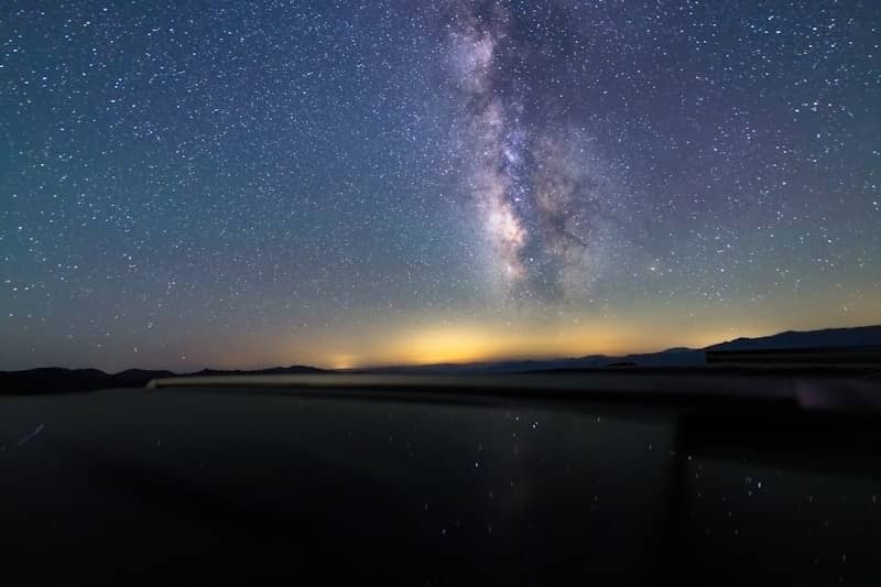 Milky way and stars reflected over a dark night landscape.