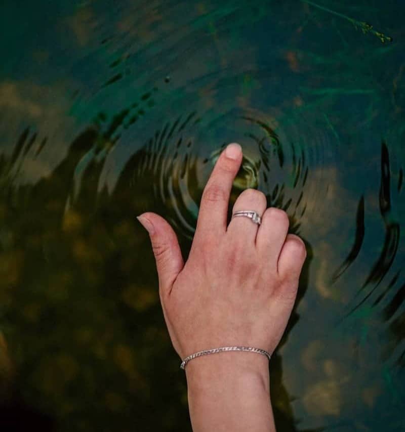 Hand touching calm water, creating ripples