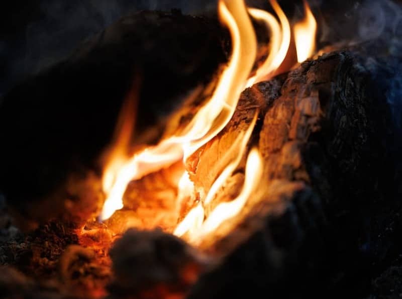 Flames dance around burning logs with wisps of smoke.