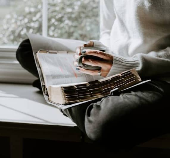 A person sitting on a window sill reading a book