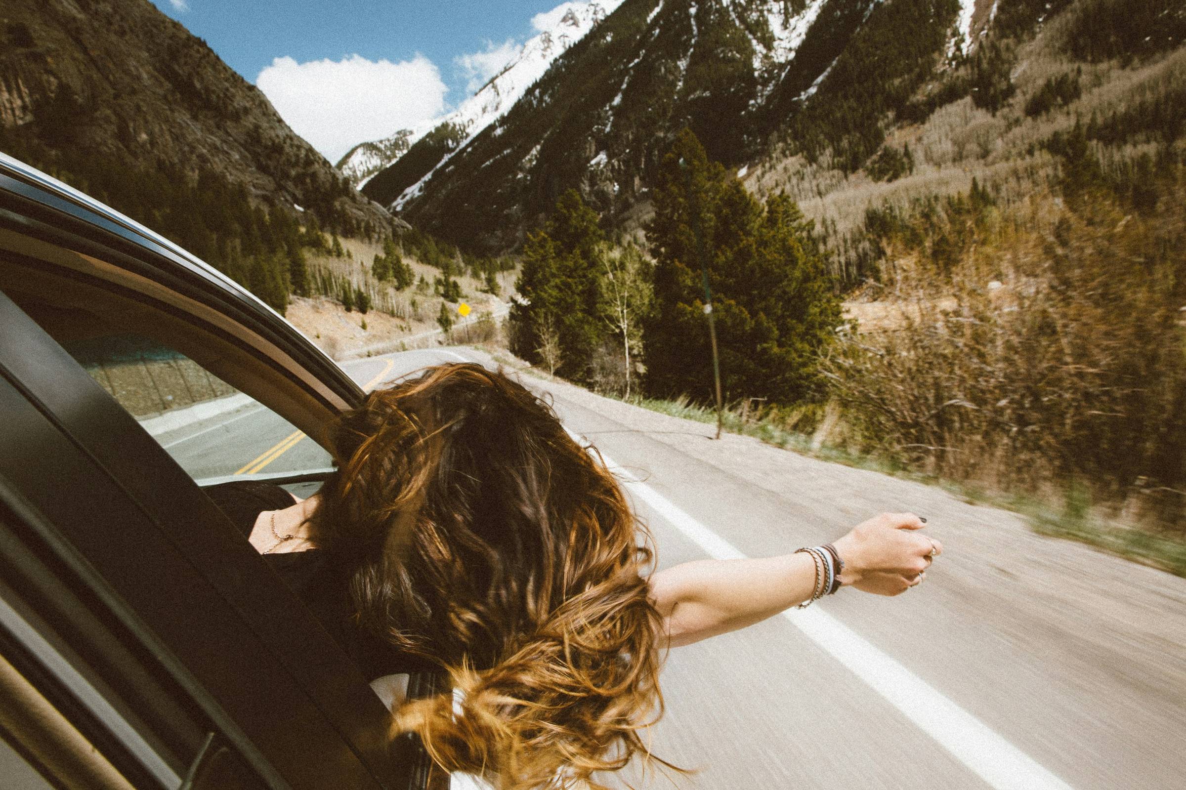 a woman in a car with her arm outside the window on a road trip