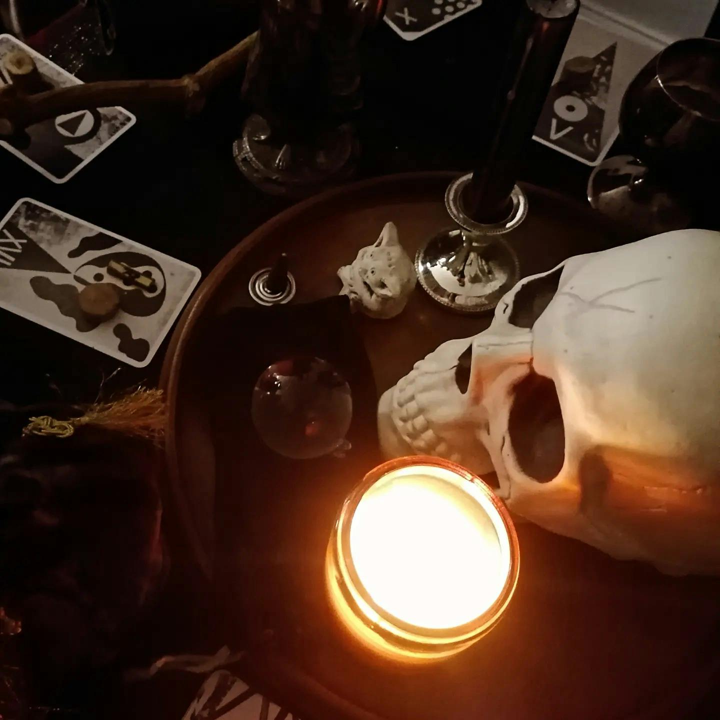 A Samhain altar with lit candle, plastic human skull, and black and white tarot cards, a small crystal ball, and incense cone - viewed from above.