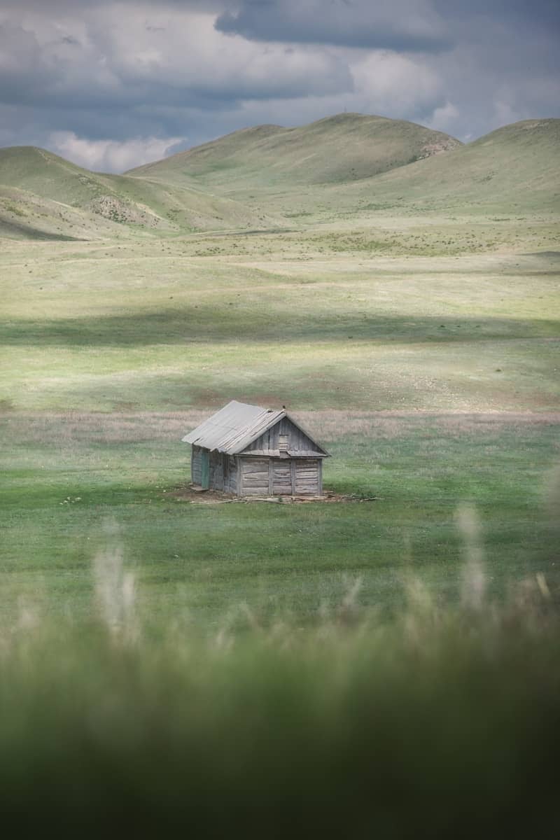 Small wooden cabin in a vast, green, rolling landscape.