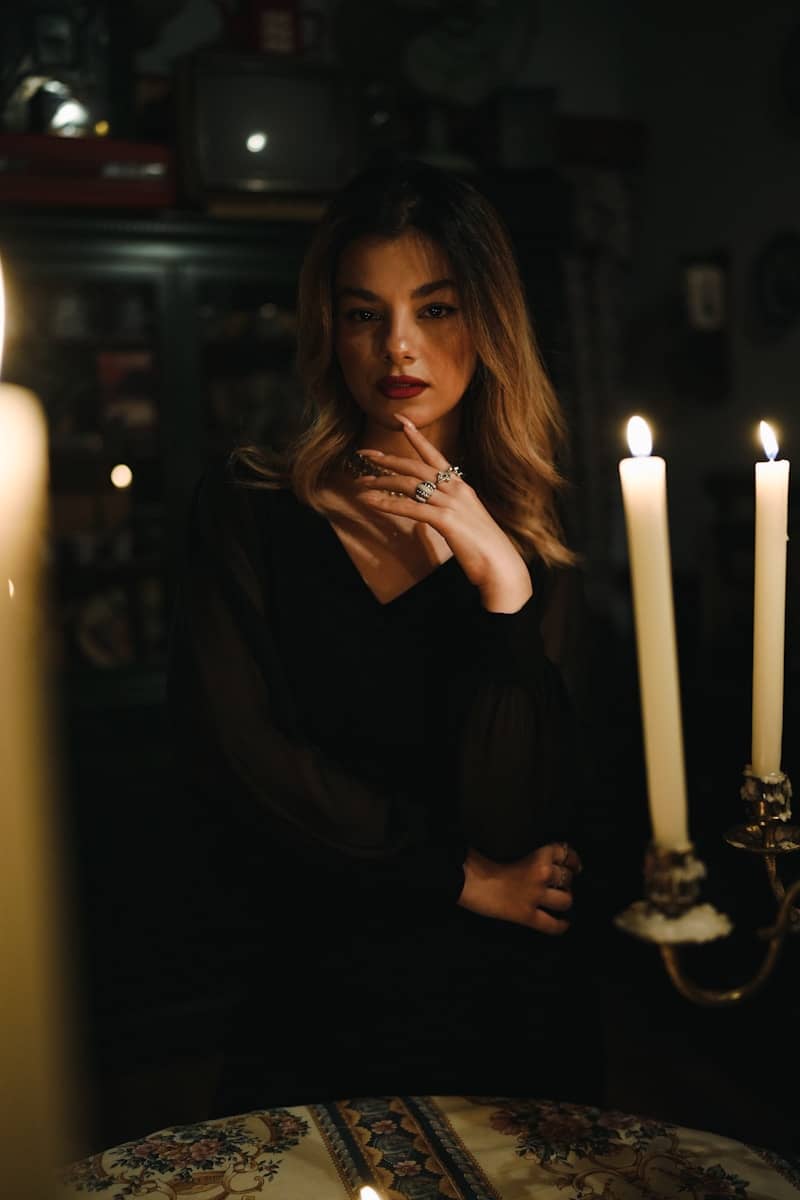 A woman in a black dress posing by candlelight in a dimly lit room