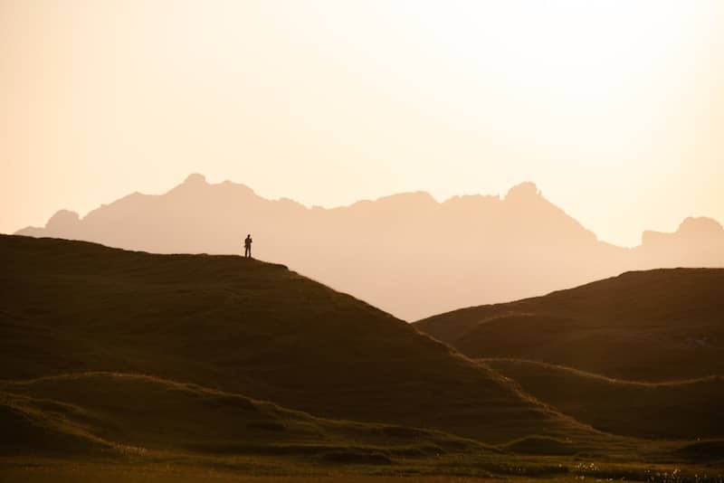A person in silhouette on a grassy hill against a warm orange sky