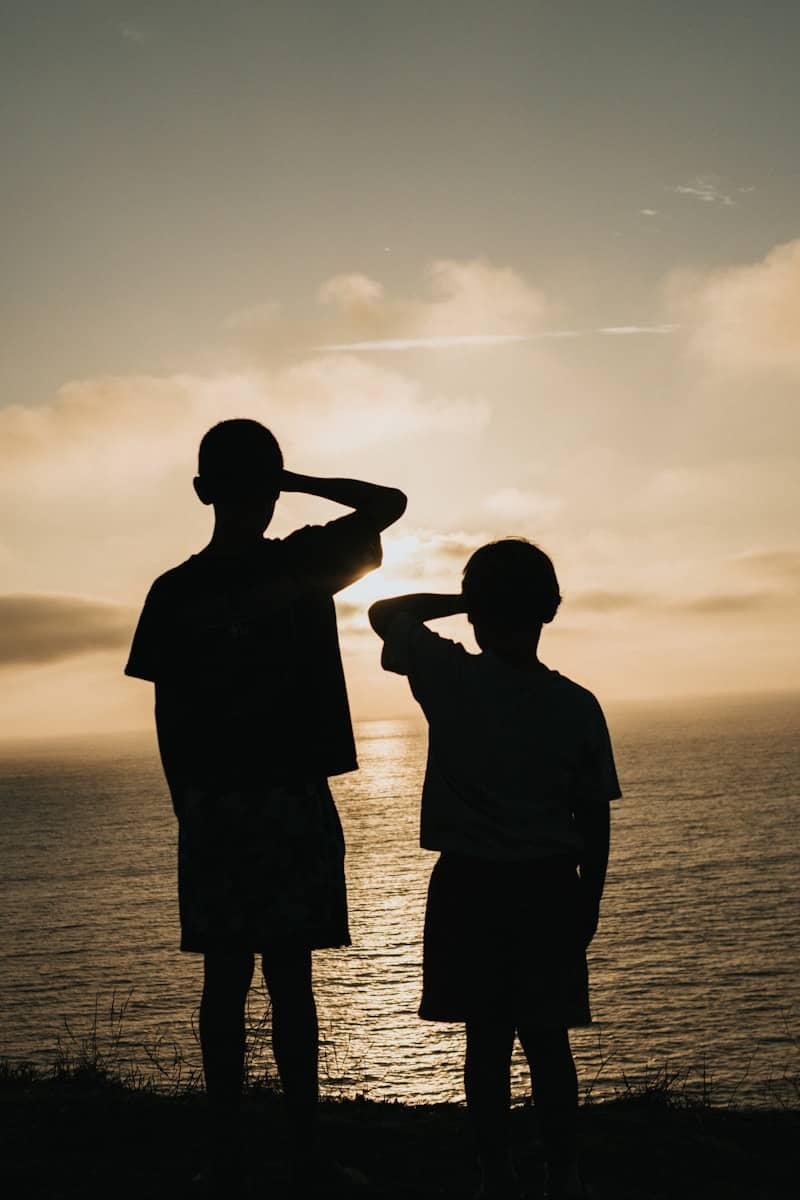 Two children silhouetted against a vibrant sunset over the ocean.