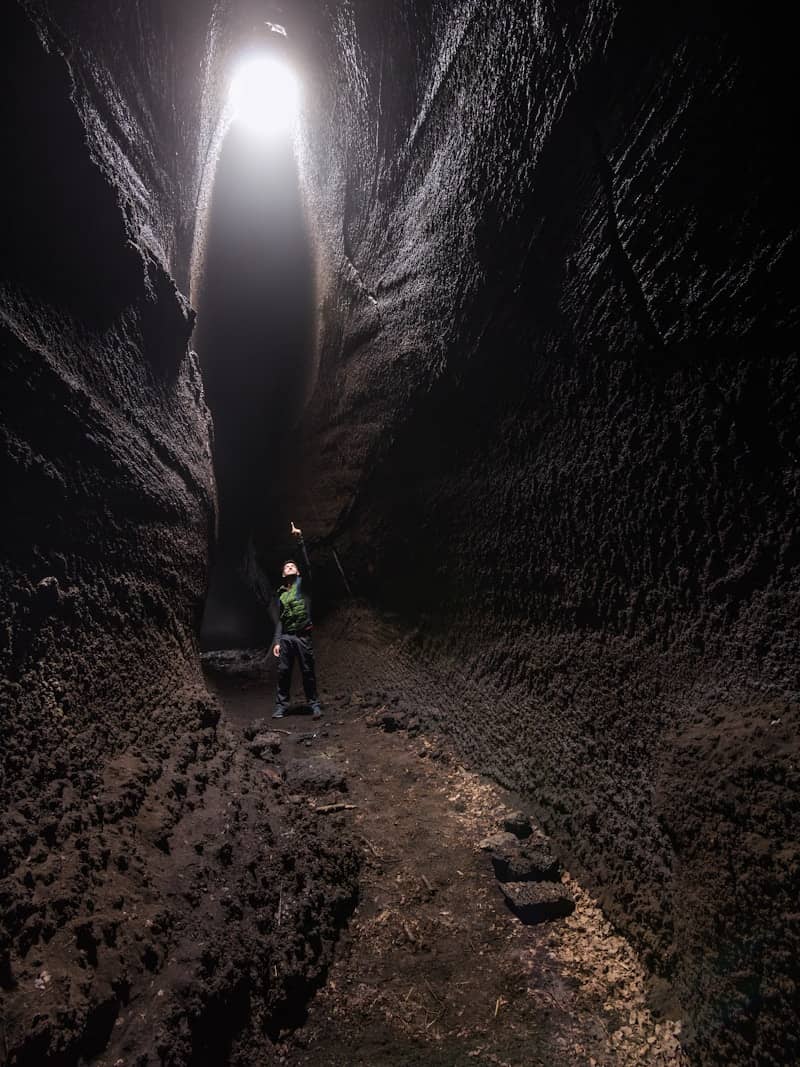 Person points up towards light in a dark cave.