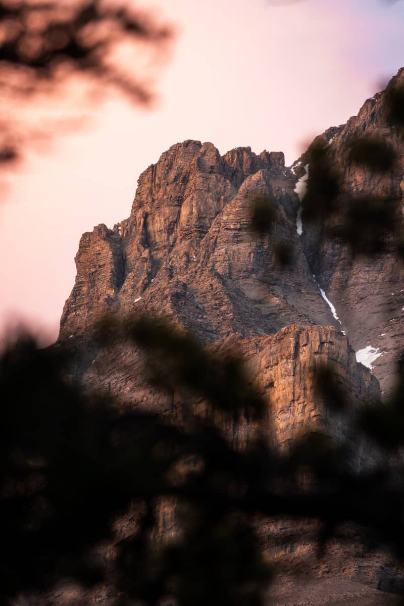 Rugged mountain peak at sunset with foreground branches.