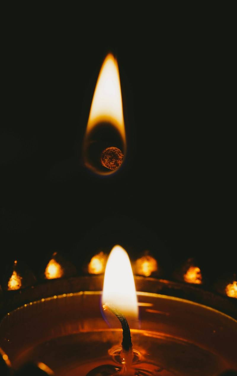 A glowing candle flame above a small floating ember in the dark