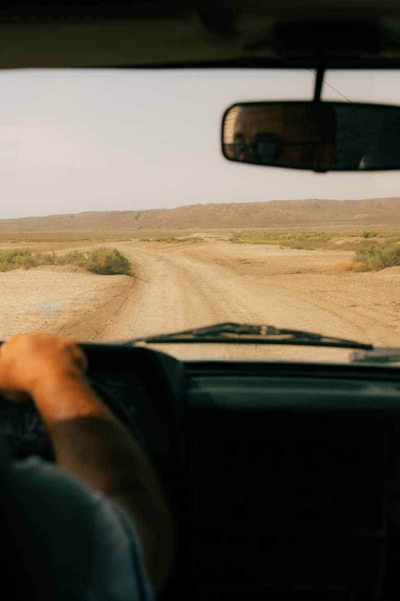 Hands on steering wheel driving on a dusty desert road.