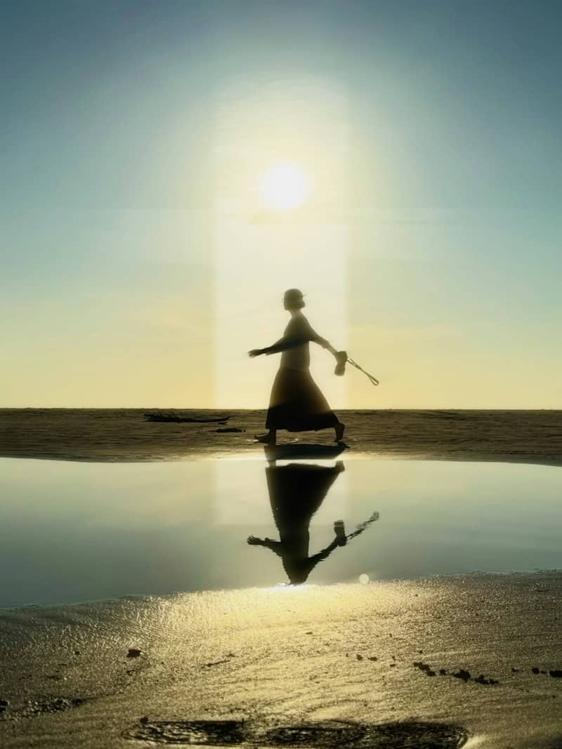 A person in silhouette walking on a beach with a reflection in a tidal pool
