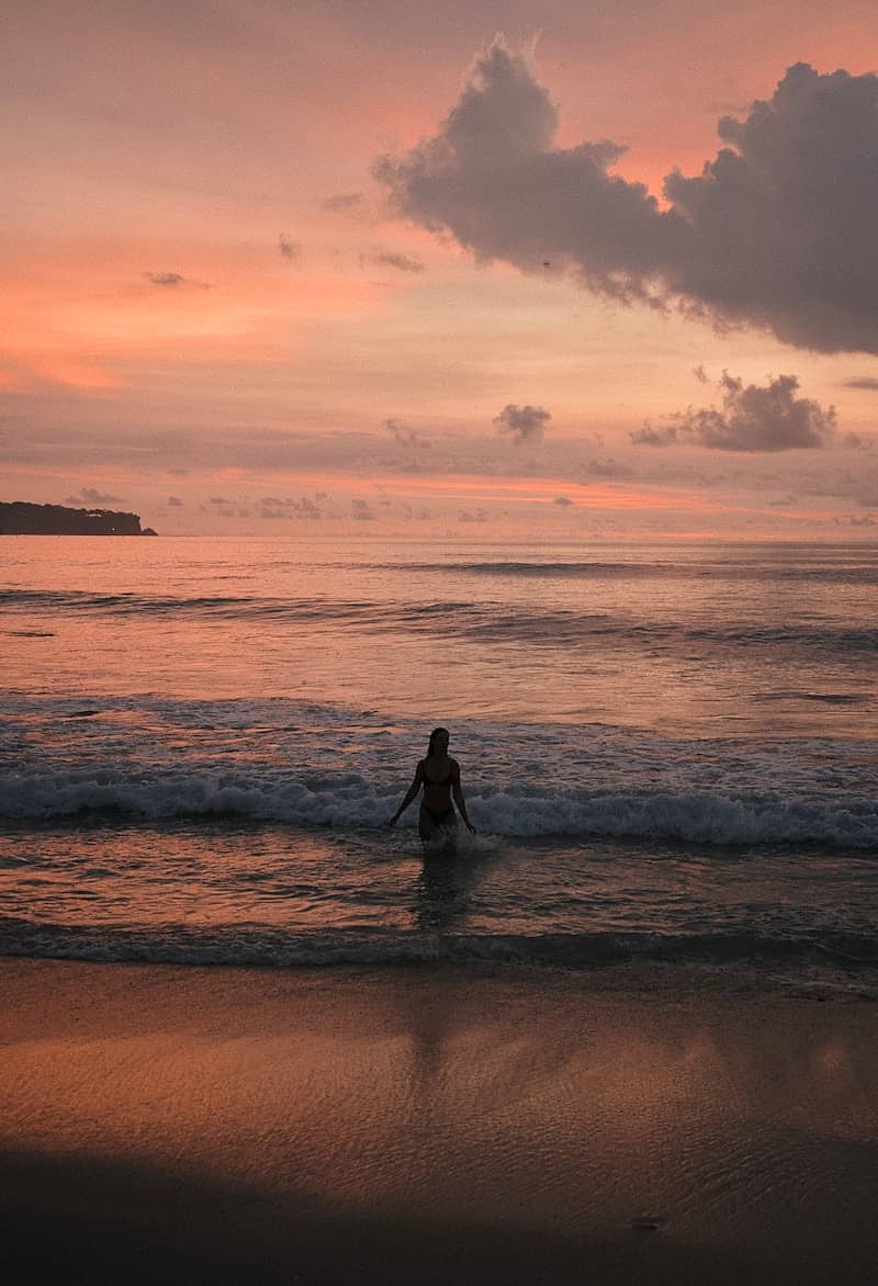 Woman in ocean during a vibrant orange and pink sunset.