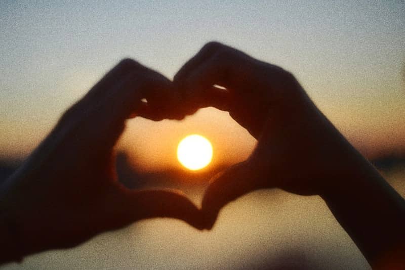 Hands forming a heart shape silhouetted against a beautiful sunset.