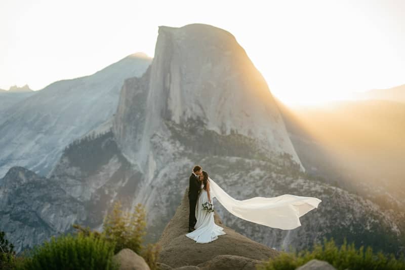 Bride and groom embrace with veil flowing in yosemite.