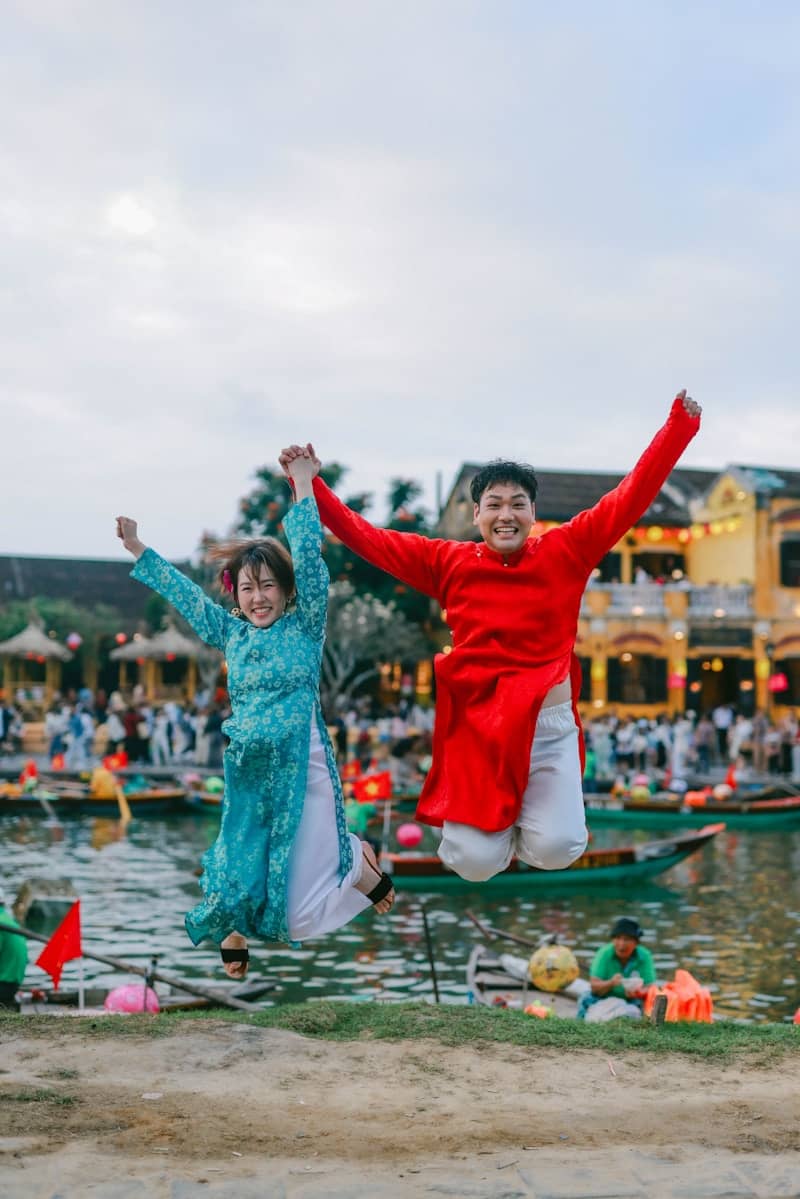 Couple in traditional outfits jumping joyfully by river
