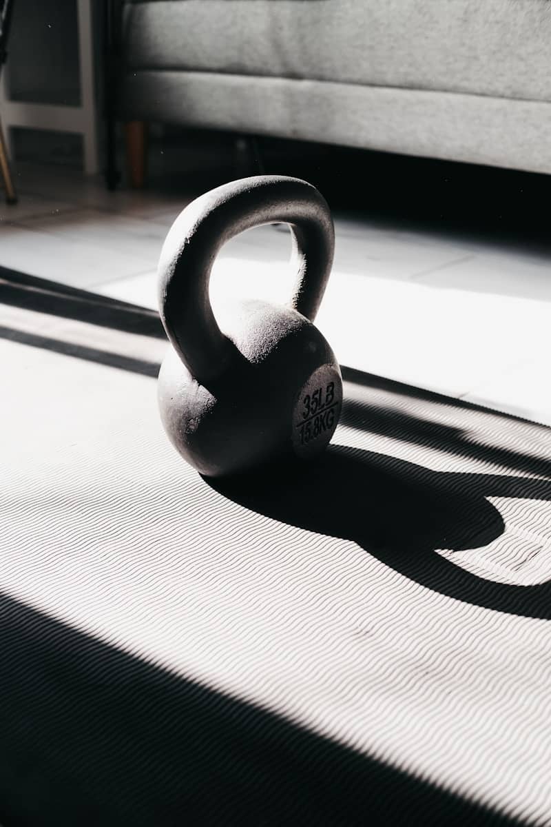 A kettlebell rests on a yoga mat in sunlight.