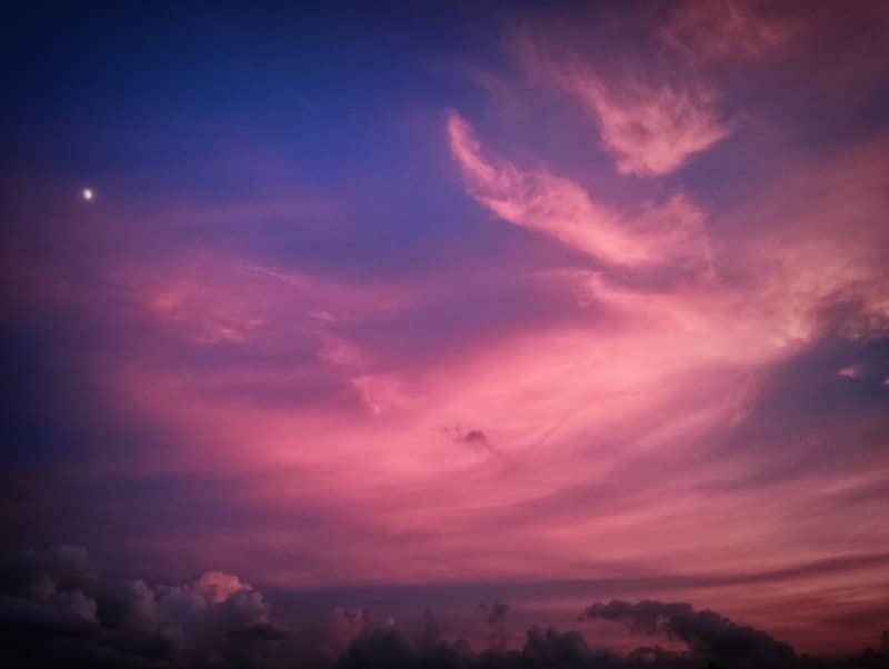 Pink and purple sunset clouds with a crescent moon.