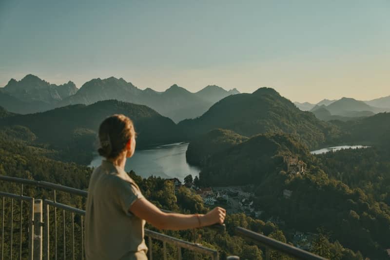 A person looking out over a lake and mountains from a metal railing