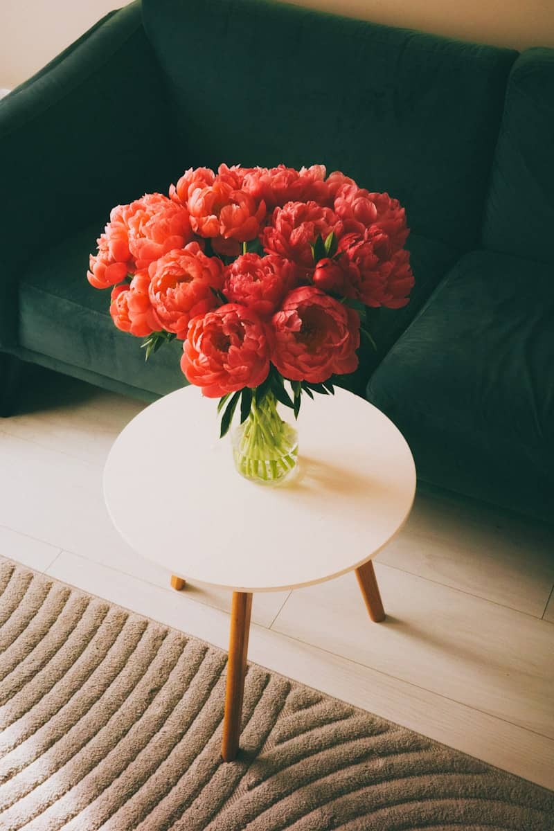 A vase of red peonies on a white table.