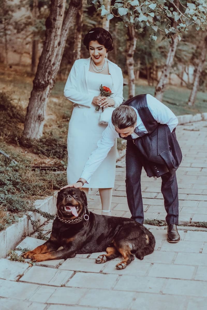 A couple petting a rottweiler dog on an outdoor path.