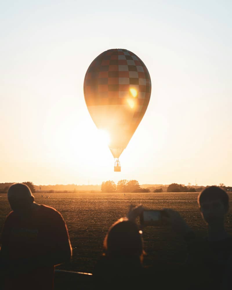 A checkered hot air balloon backlit by low sun over a grassy field