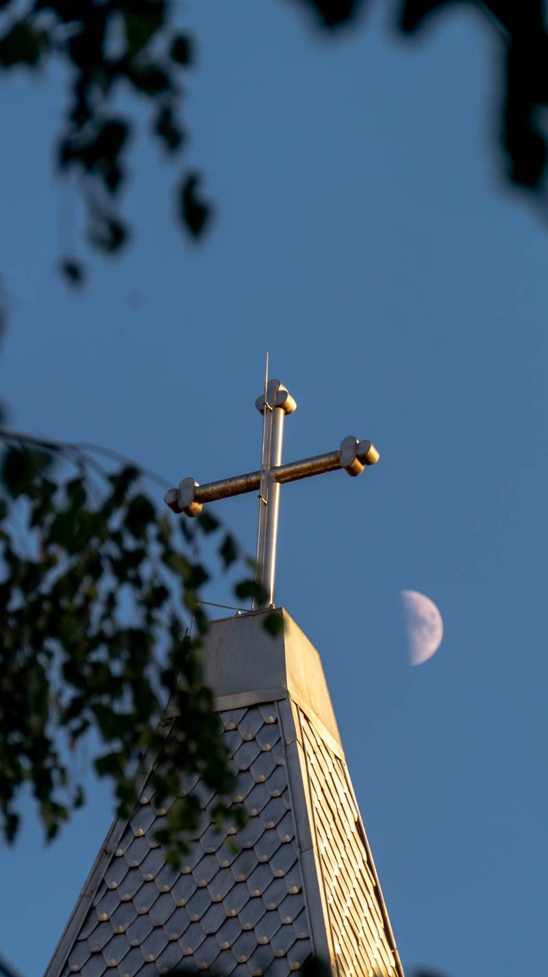 A church cross is near the moon in the sky.