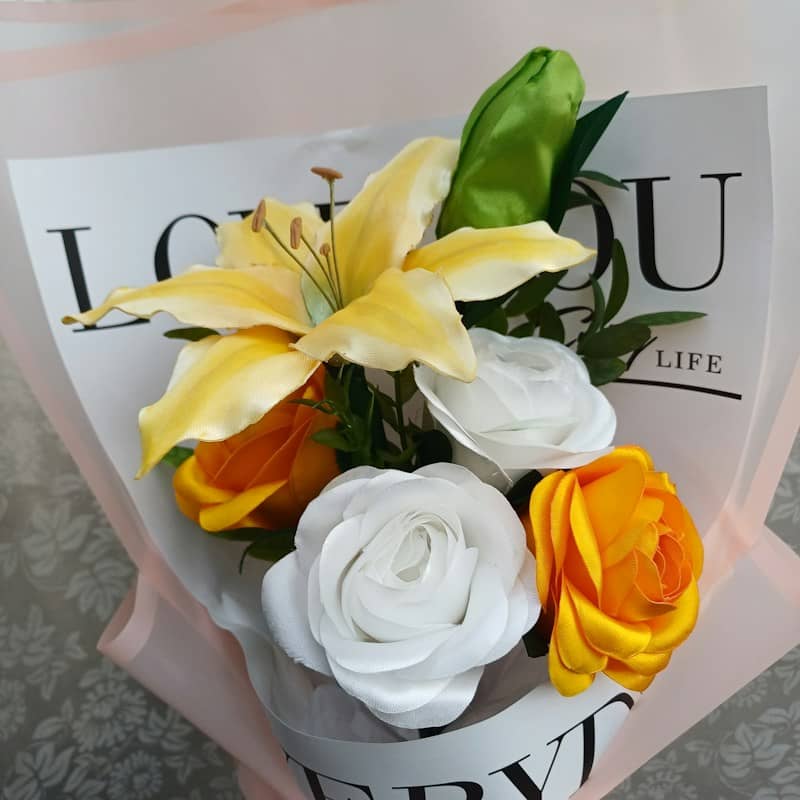 A bouquet of yellow lilies and white and orange roses in decorative paper