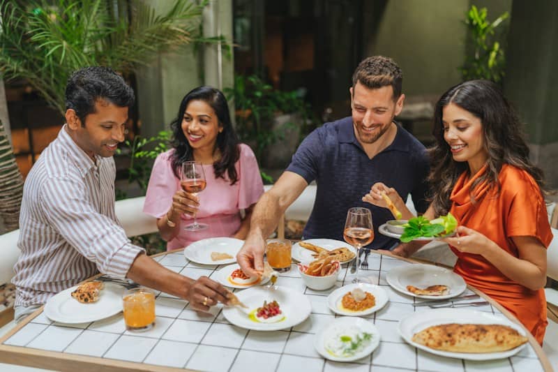 Four adults sharing small plates and drinks at a table in a restaurant