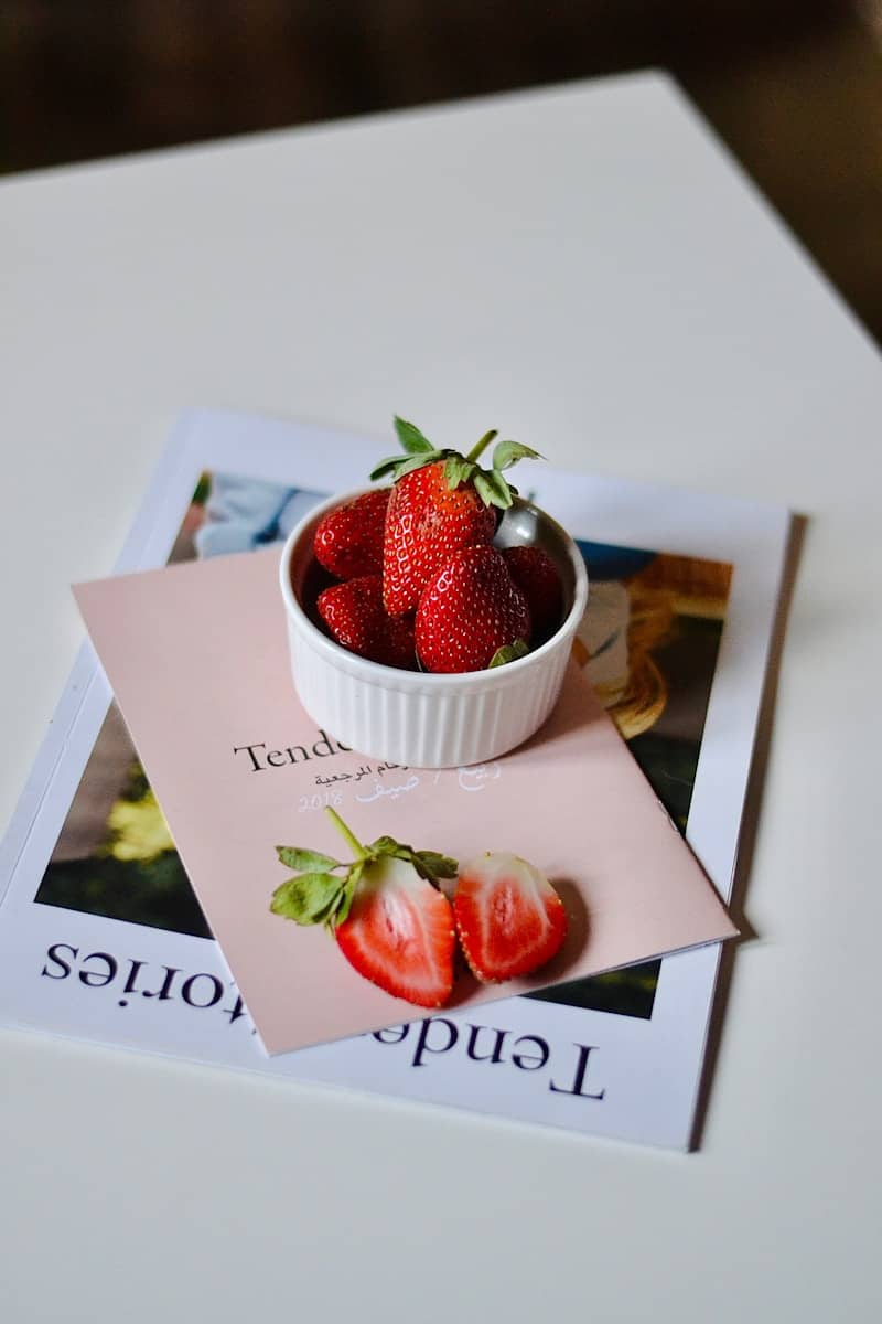 Fresh strawberries in a white dish on a magazine.