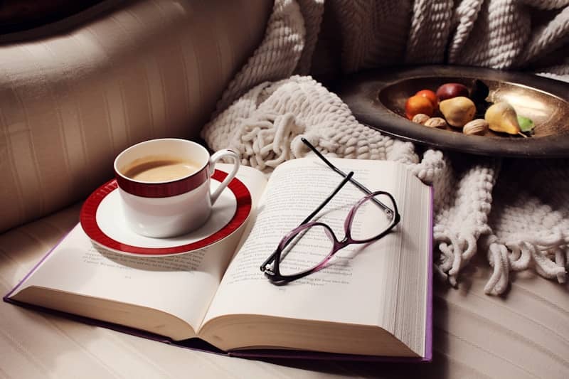 An open book, coffee, and eyeglasses on a cozy couch.