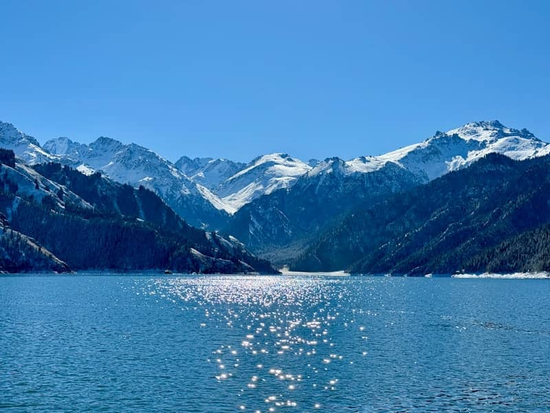 Snow-capped mountains reflect on a sparkling blue lake.