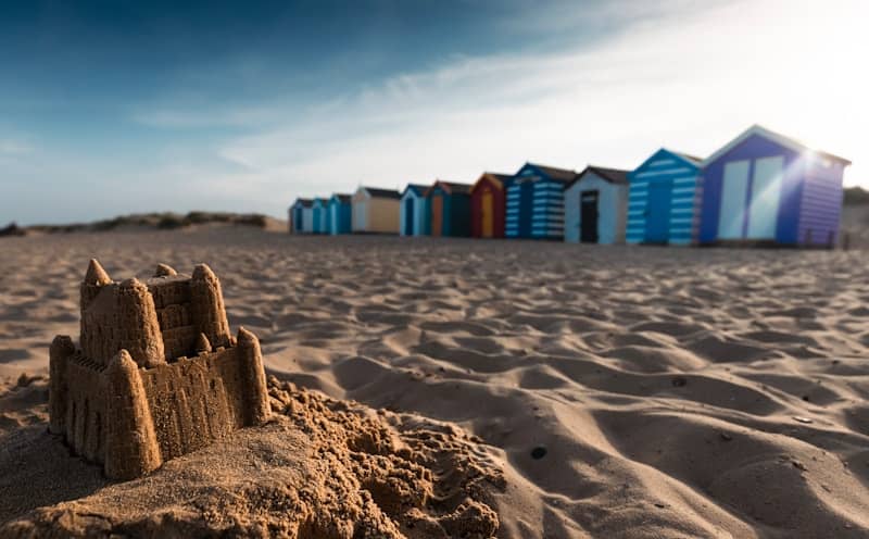 A sandcastle on a sunny beach with colorful huts.
