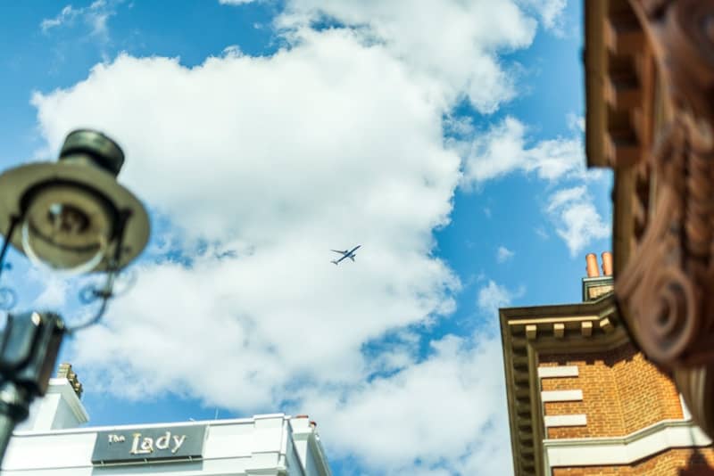 An airplane flies through blue skies high above the buildings in London