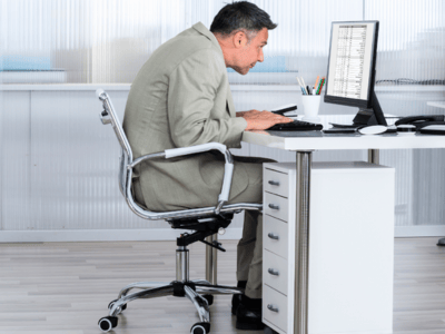 Man at desk slumped and staring into his monitor. He is too big for the chair he's in.